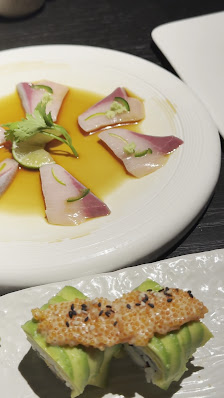 The image shows a plated dish consisting of two pieces of sushi topped with what appears to be sesame seeds and green herbs, served on a white rectang