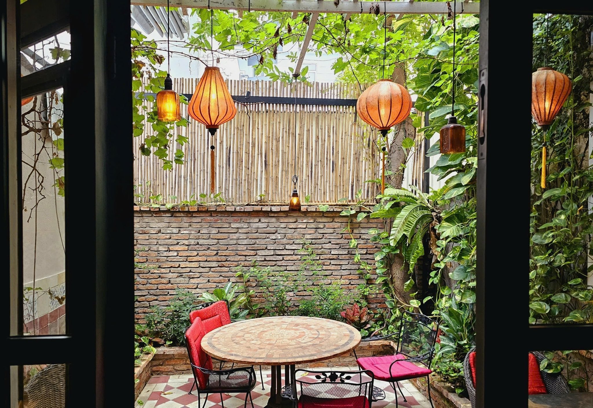 This image depicts an outdoor seating area within a venue in Thao Dien, Saigon. The space is adorned with hanging lanterns that emit a warm glow and c