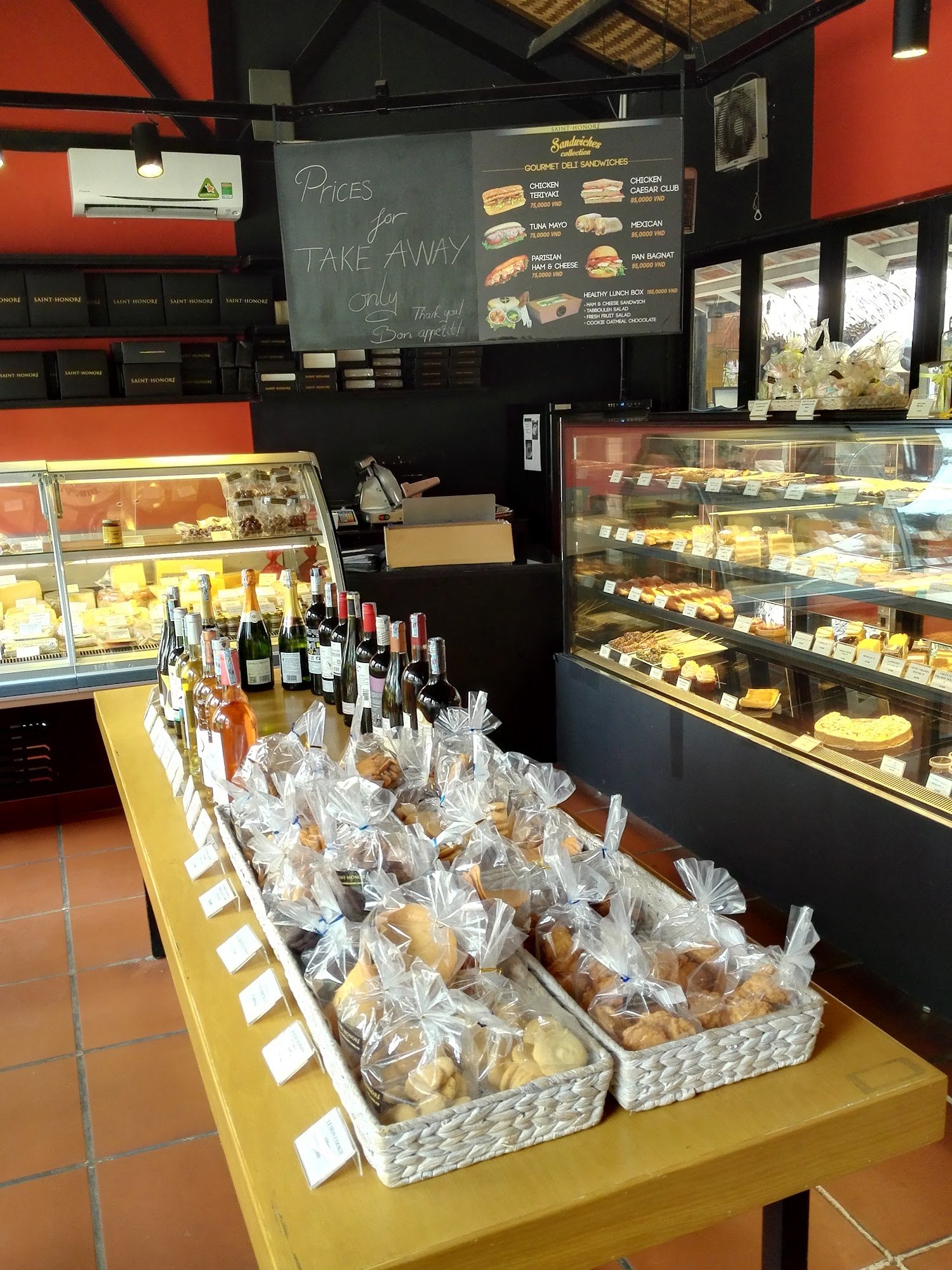 The image shows an interior view of a bakery or café that offers various food items and drinks for sale. The counter displays baked goods, pastries, c
