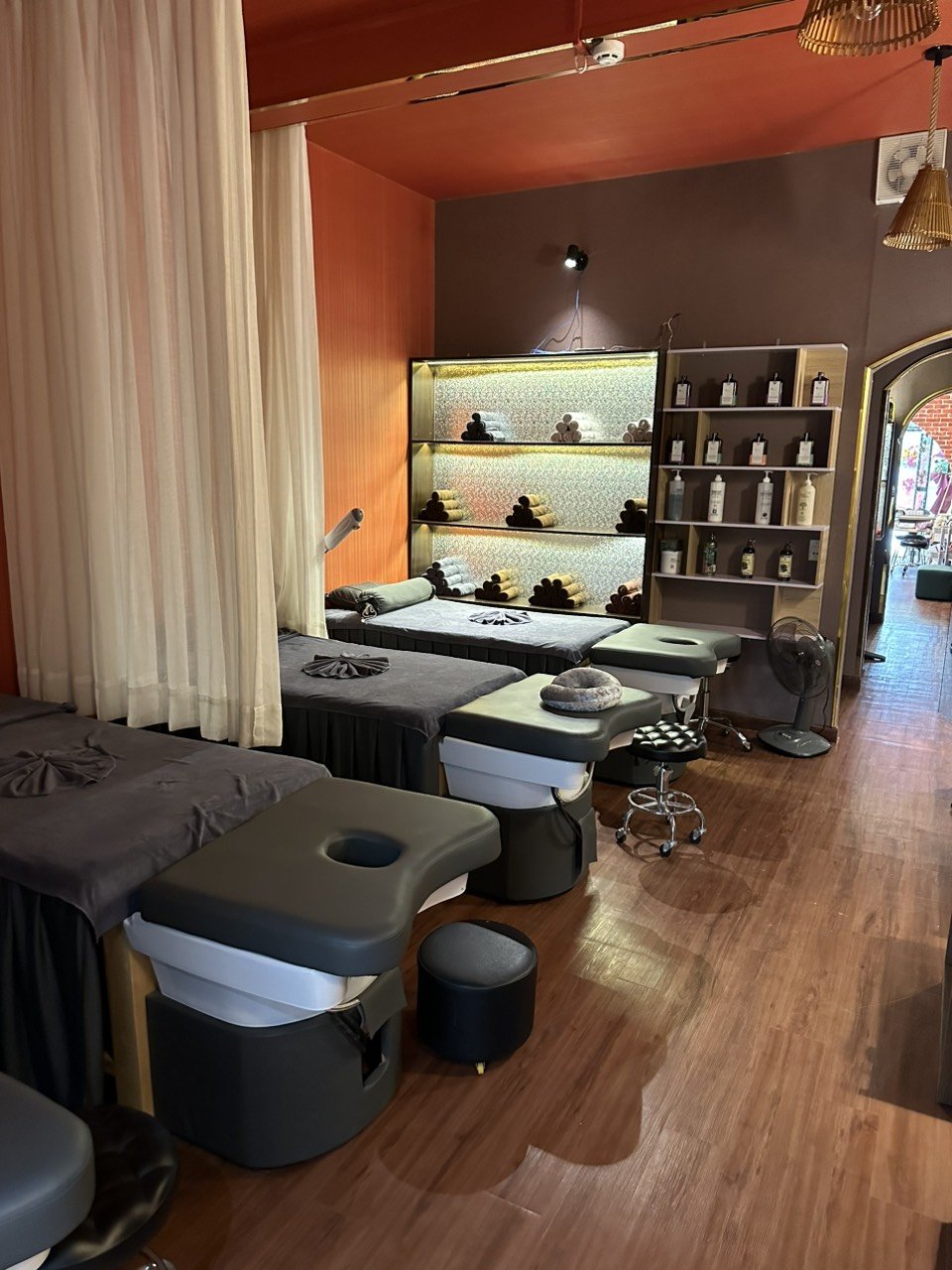The image depicts an interior view of a modern spa or wellness center featuring multiple treatment tables with dark-colored linens and accessories suc