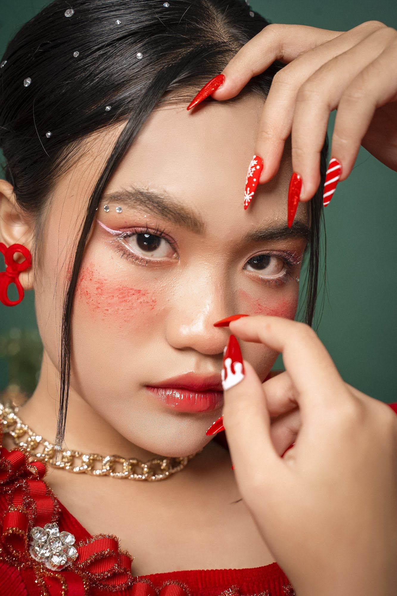 A close-up portrait of a person adorned in festive red and gold accessories, including nail art with holiday motifs.