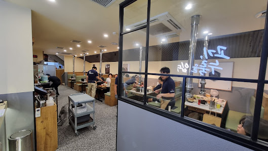The image shows an interior view of a restaurant or cafe where customers are seated at tables with food and drinks in front of them, while staff membe
