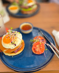 A plated dish consisting of a burger topped with an egg and garnished with microgreens on the side, accompanied by sliced tomatoes and served on a blu