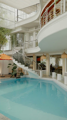 The image shows an indoor swimming pool area within a multi-level building. The architecture includes modern design elements such as glass railings, w
