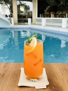 A refreshing orange cocktail garnished with a sprig of rosemary and lemon slice is placed on a wooden table by the poolside at Thao Dien, Saigon.
