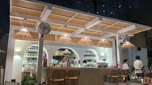 The image shows an interior view of a bar area at night time in Thao Dien, Saigon. The establishment has a modern and cozy ambiance with wooden beams 