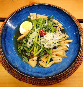 A colorful salad dish served on a blue plate, featuring an assortment of vegetables such as green onions and leafy greens, topped with sliced mushroom