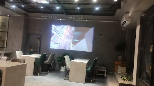 The image shows an interior space that appears modern and well-lit. There is a large screen displaying what seems to be aerial footage of buildings, w