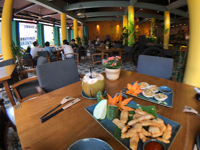 The image depicts the interior of a restaurant in Thao Dien, Saigon. It features a wooden table with various dishes, including a platter of spring rol