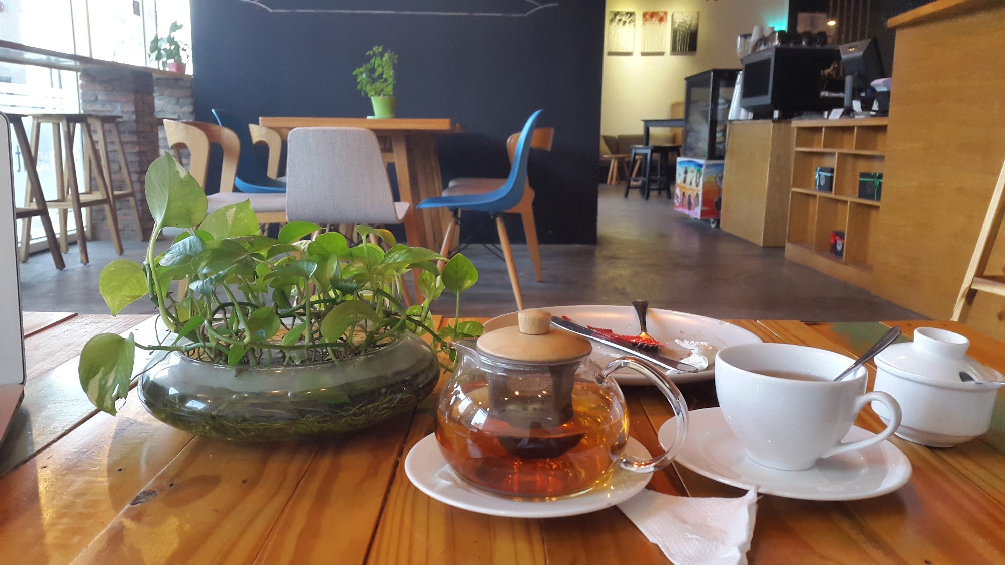 The image shows a cozy interior of what appears to be a café or restaurant in Thao Dien, Saigon. The focus is on a wooden table with various items inc