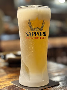 A close-up of a frothy glass of Sapporo beer on a wooden surface.