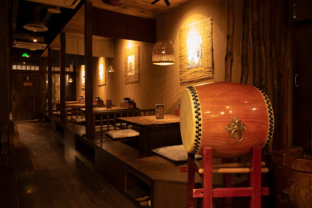 The image depicts an interior setting of a restaurant or bar that has wooden elements and traditional decor items such as lanterns, a drum on display,