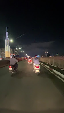 A nighttime scene of motorcycles on a road in an urban area.