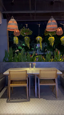 The image shows an interior view of a modern restaurant or cafe at night. The space features wooden chairs and tables with woven seats, set against a 