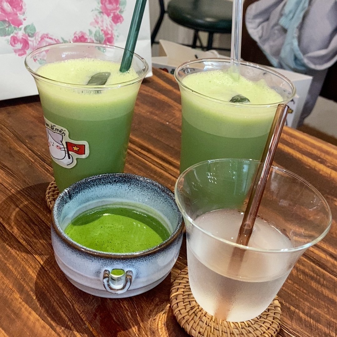 The image shows a collection of green-colored drinks in various containers on a wooden surface.