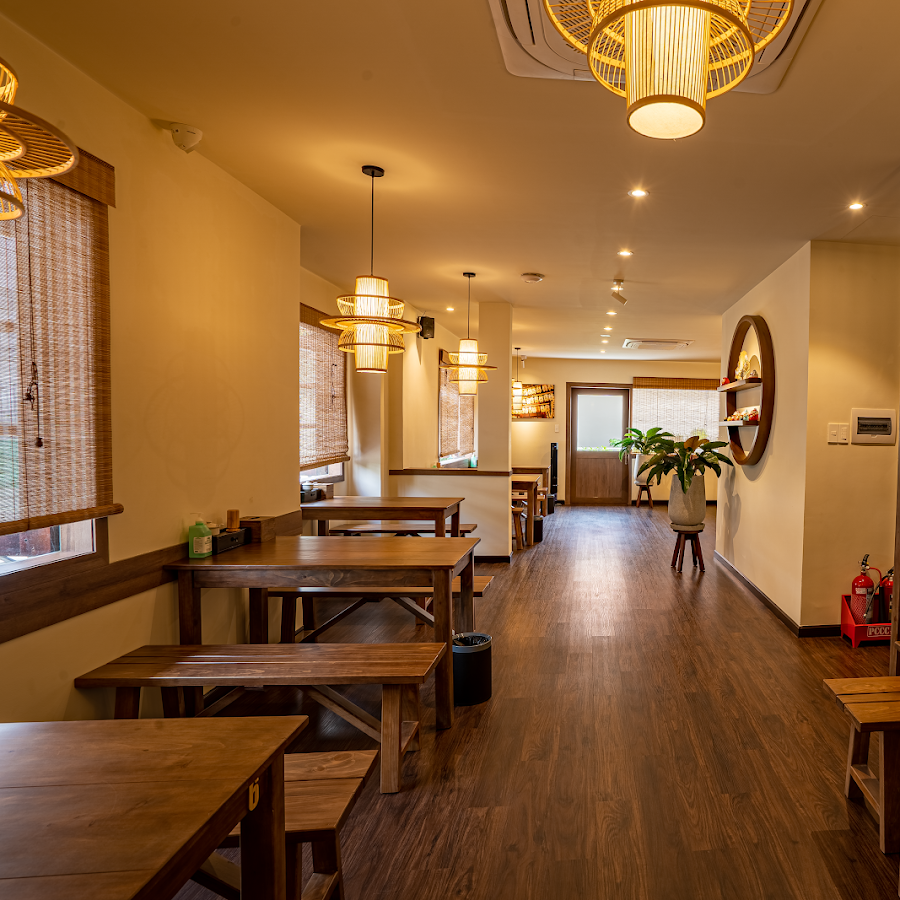 The image depicts the interior of a venue in Thao Dien, Saigon. It features wooden tables and benches arranged along the walls, with woven bamboo-styl