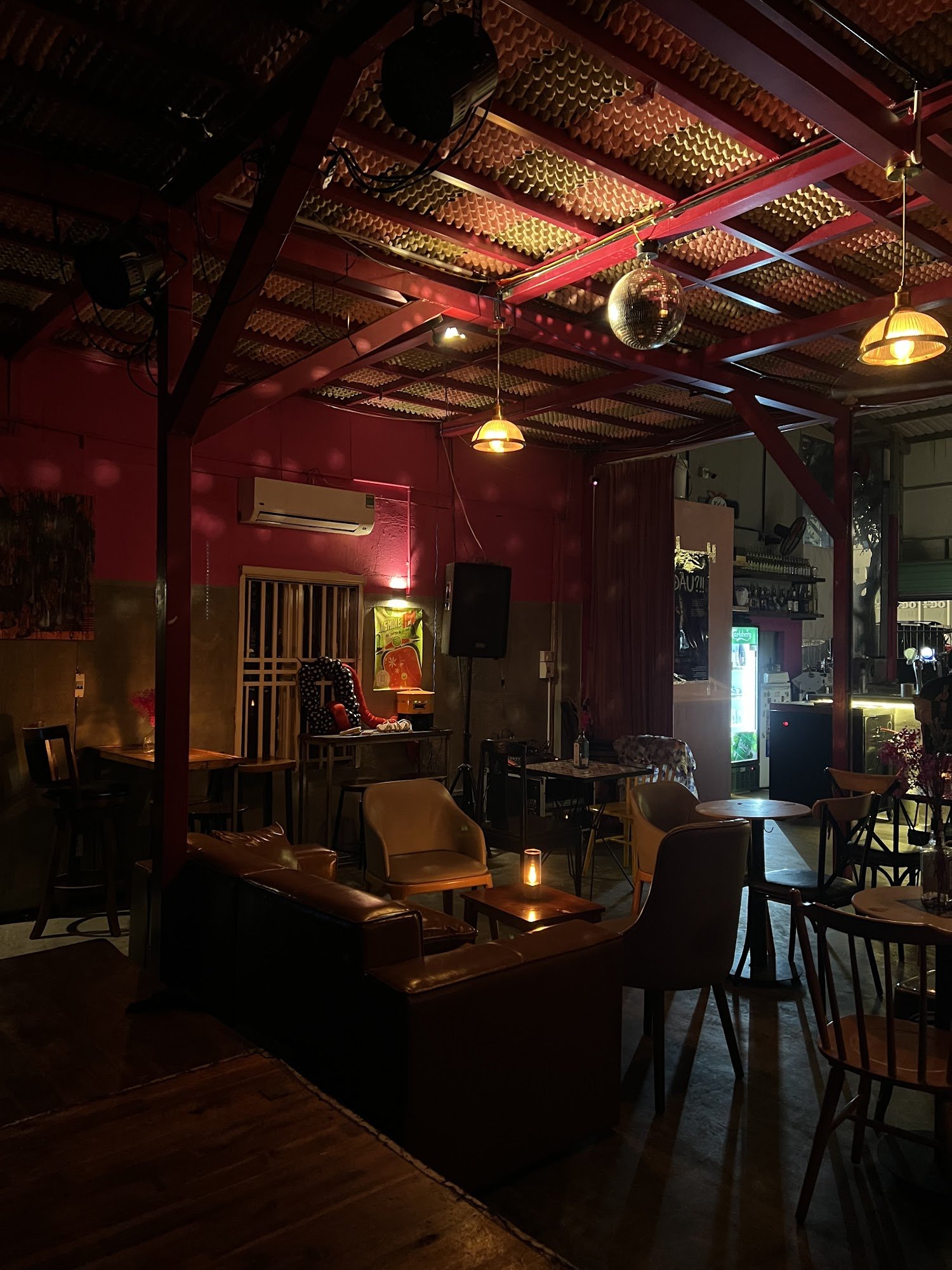 The image depicts an indoor venue with a warm and cozy ambiance. The space features red walls and wooden flooring, creating a rustic atmosphere. There