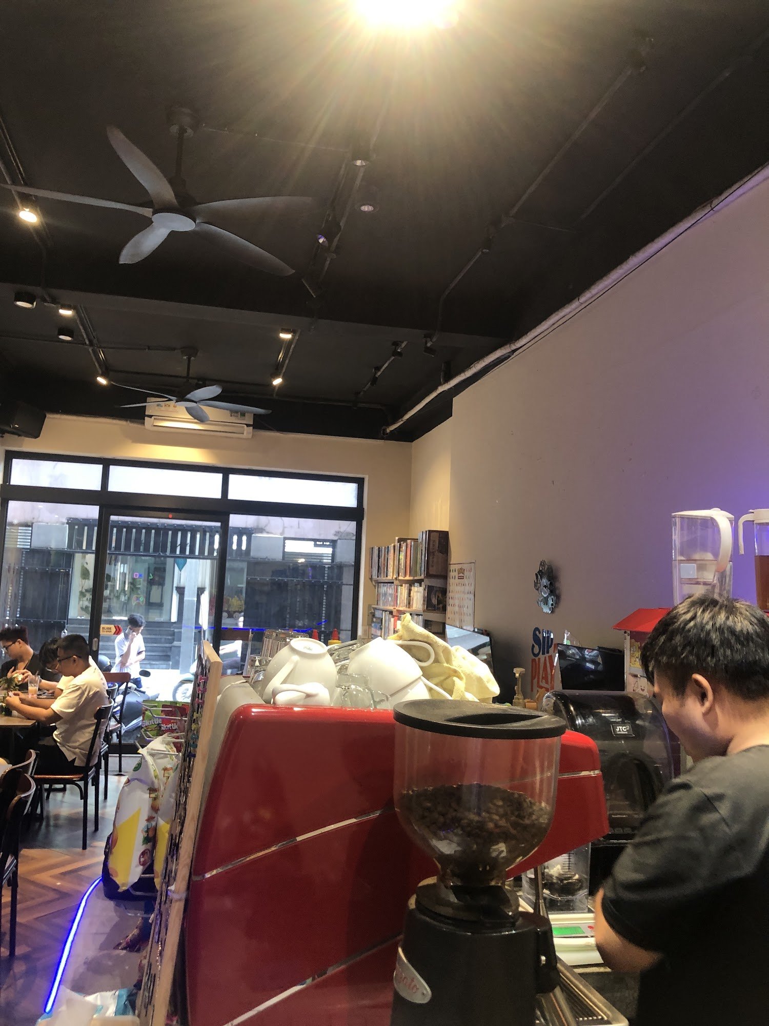 The image depicts the interior of a café in Thao Dien, Saigon. Key elements include a red counter with coffee equipment (e.g., a coffee grinder filled