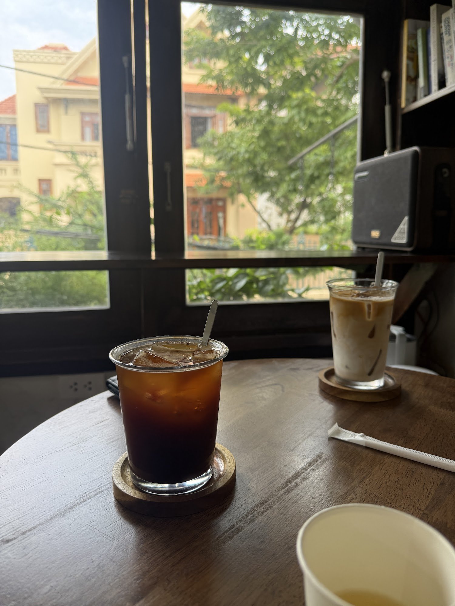 The image shows a cozy interior setting of what appears to be a café or restaurant with two glasses on the table containing cold beverages, likely cof