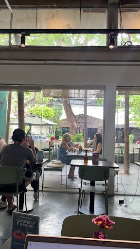 The image shows an interior view of a cafe or restaurant in Thao Dien, Saigon. Patrons are seated at tables enjoying drinks and conversations under la