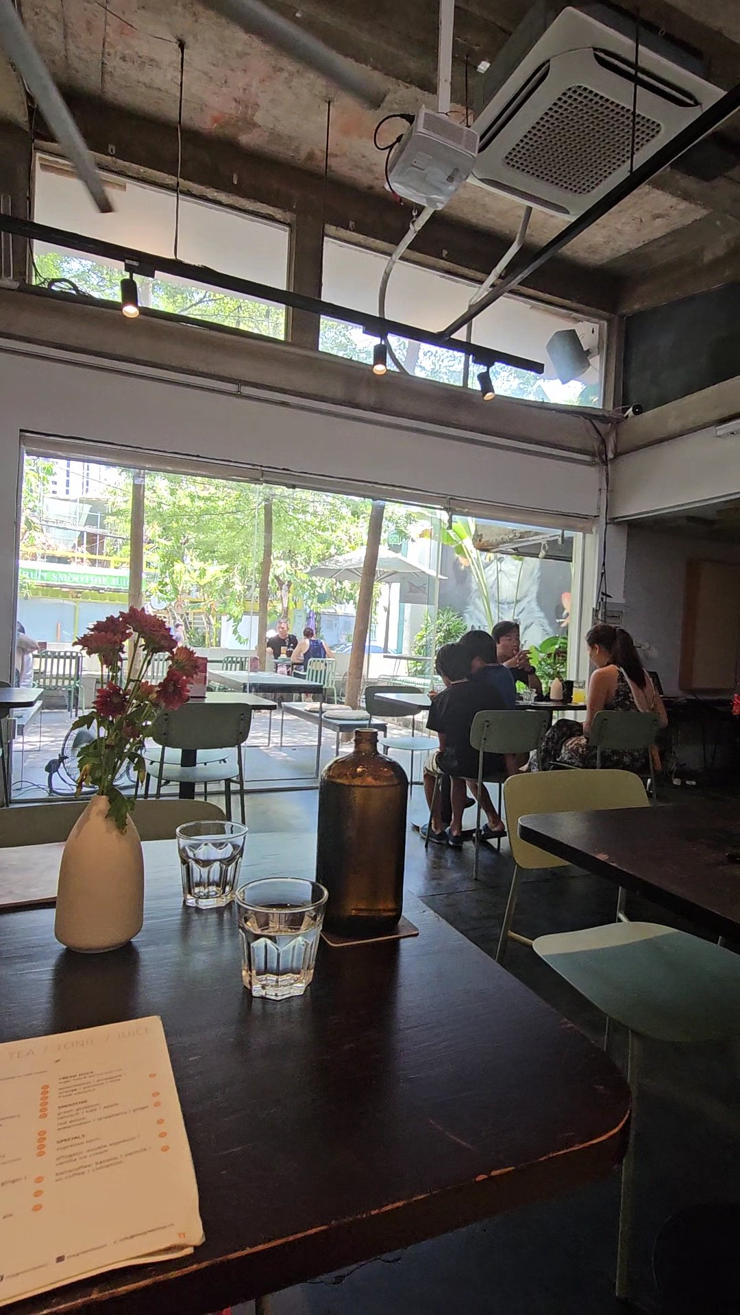 The image shows an interior view of a casual dining establishment in Thao Dien, Saigon. The space is well-lit with natural light coming through large 