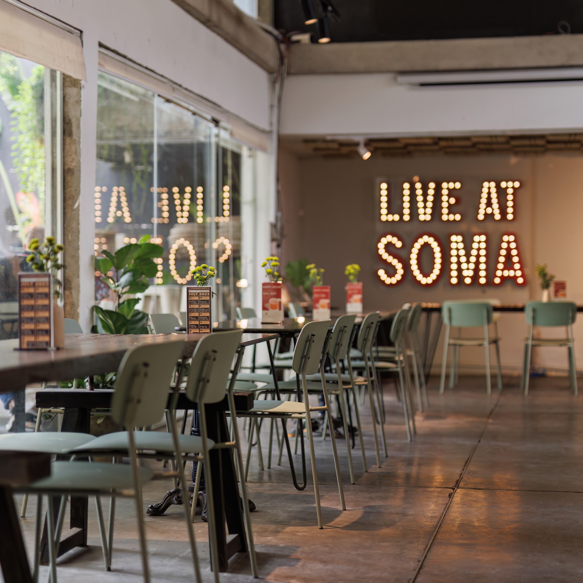 The image depicts an indoor dining area of a venue named 'Live at Soma'. The space is modern with exposed brickwork and large windows that allow natur