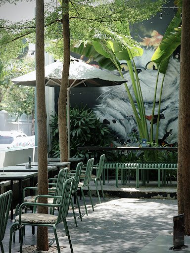 The image depicts an outdoor seating area of a restaurant or café in Thao Dien, Saigon. The setting is characterized by green metal chairs and tables 