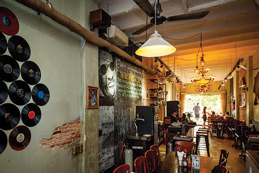 The image depicts the interior of a venue in Thao Dien, Saigon. It features exposed brick walls with visible patches, vintage vinyl records mounted on
