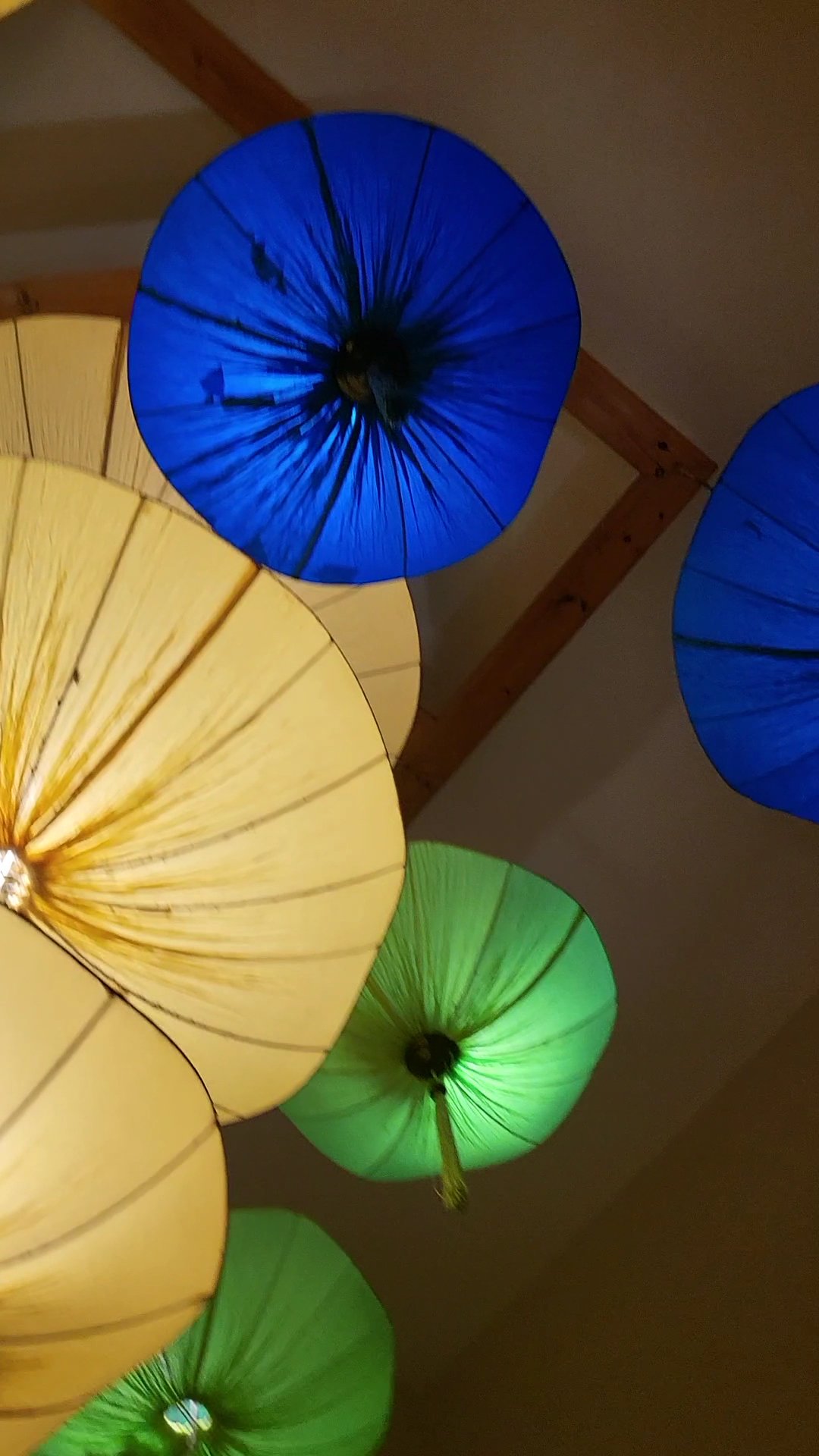 The image features vibrant, flower-shaped ceiling fixtures in blue, yellow, and green hues. Each fixture has a radial pattern with visible seams, rese