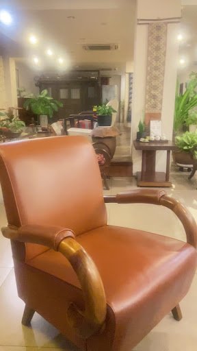 The image shows a well-lit interior space featuring an elegant brown leather armchair with wooden accents in the foreground. In the background, there 