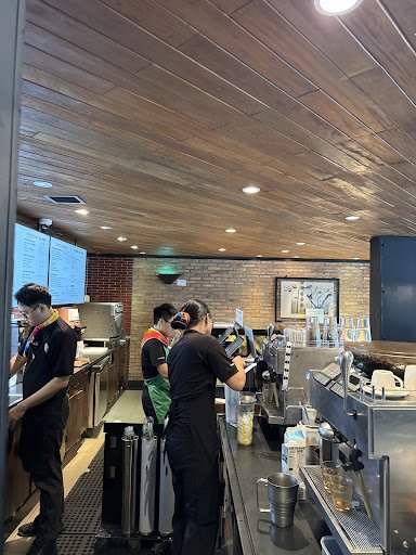 The image depicts the interior of a café in Thao Dien, Saigon. It features a wooden ceiling with recessed lighting, a brick wall backdrop, and multipl