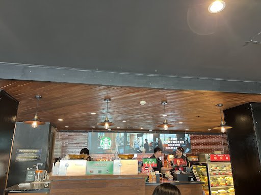 The image depicts the interior of a Starbucks coffee shop located in Thao Dien, Saigon. It features a wooden ceiling with hanging pendant lights, a co