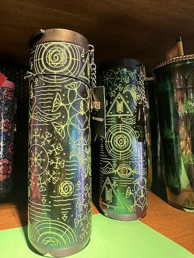 Three cylindrical containers with intricate glowing yellow designs on a dark background, placed on a green surface. Each container has a chain attachm
