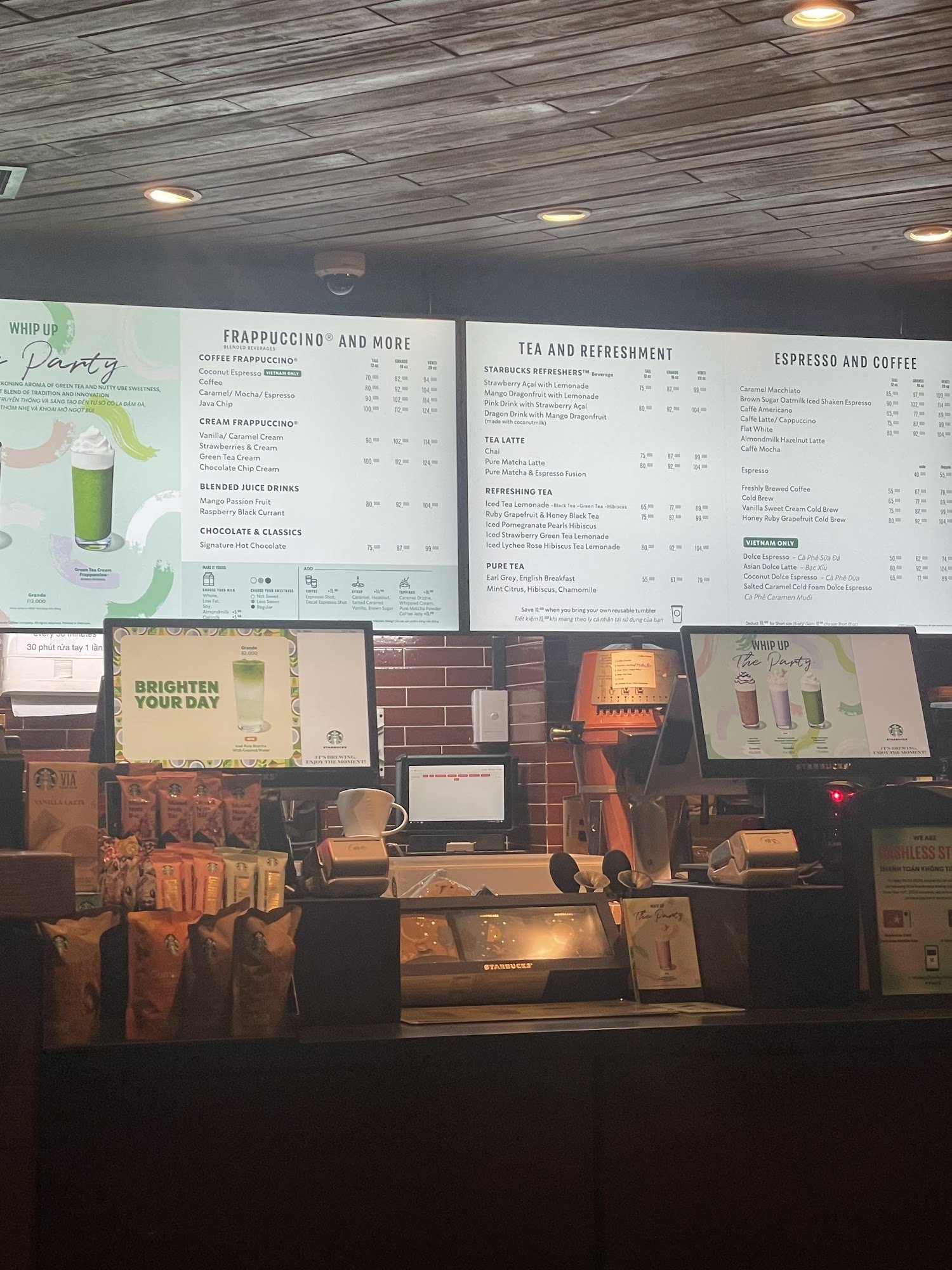 The image depicts the interior of a Starbucks store in Thao Dien, Saigon. It features a large menu board with sections for 'WHIP UP The Party', 'FRAPP
