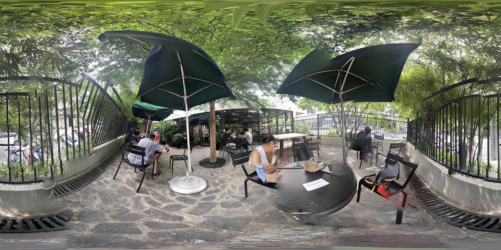 The image depicts an outdoor seating area of a venue in Thao Dien, Saigon. It features stone-paved ground with black metal chairs and round tables sha