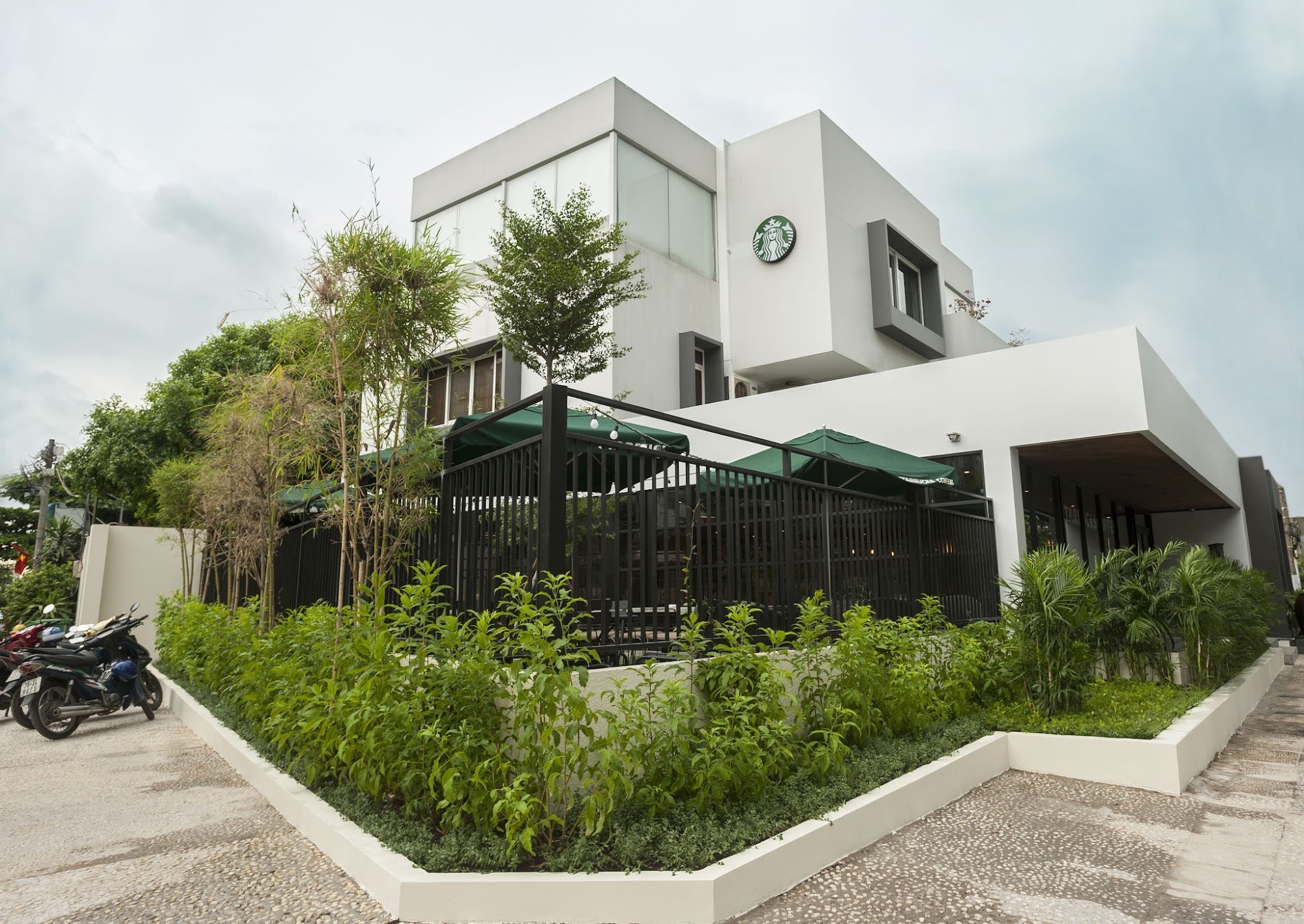 The image depicts the exterior of a Starbucks store located in Thao Dien, Saigon. The building features a modern, minimalist design with white and gra