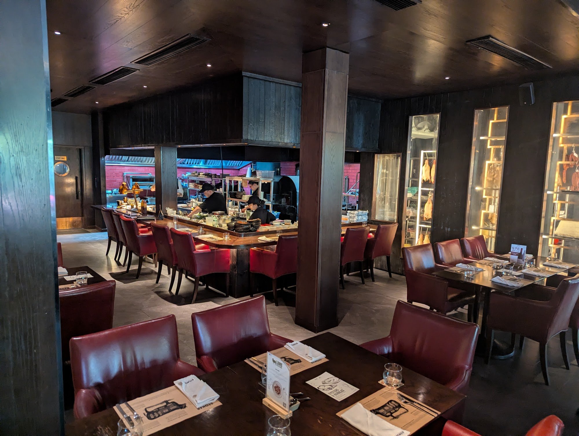 The image depicts the interior of a restaurant in Thao Dien, Saigon. It features dark wooden walls and ceiling, red leather chairs, and dark wooden ta