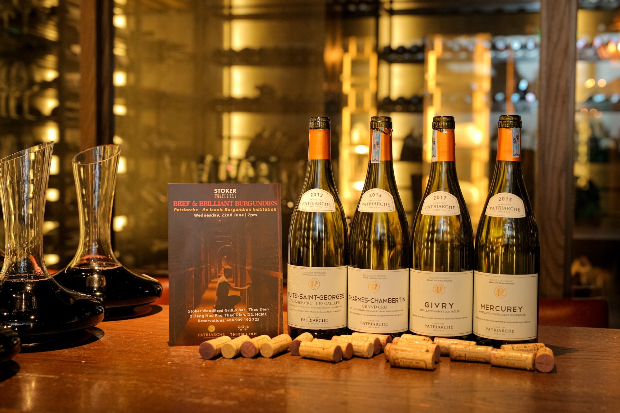 The image shows a selection of wine bottles and corks on a wooden surface in what appears to be an upscale bar or restaurant setting, with golden-hued