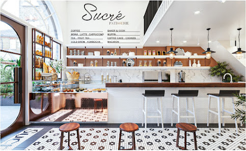 The image shows a modern and stylish interior of a cafe named 'Sucre Patisserie'. The space features an open-plan layout with a counter area where var