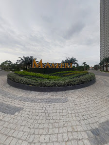 The image shows a roundabout area featuring the large sign 'MASTERI' in bold letters with an ornate design, surrounded by neatly trimmed hedges and pa