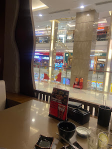 A restaurant interior with a dining table set for service, featuring a menu, bowls, chopsticks, and a view of a multi-level shopping mall through larg