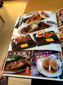 A person is holding a menu showcasing various Japanese dishes such as grilled meats and seafood.