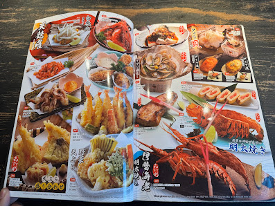 The image shows an open magazine or book displaying a variety of Japanese cuisine items such as sushi rolls, tempura shrimp, prawns, lobster tails, an