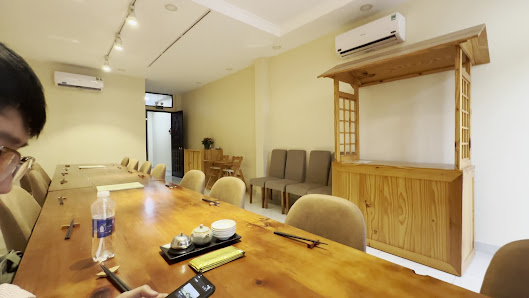 A spacious meeting or conference room with a long wooden table, beige chairs, a wooden counter structure with lattice design, air conditioning units, 