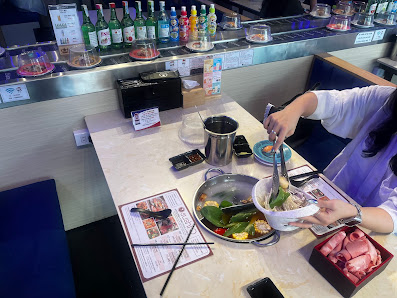 The image depicts an interior scene of a restaurant in Thao Dien, Saigon. A person wearing a purple apron is actively preparing food at a counter. The