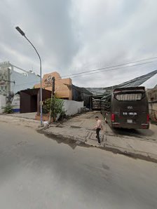 An outdoor street scene in Thao Dien, Saigon, featuring a parked bus, a person walking with a bicycle, buildings with corrugated metal roofs, a street