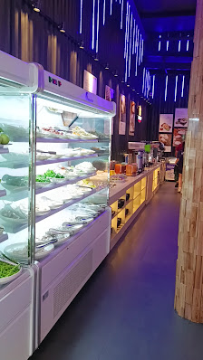 The image depicts the interior of a modern food venue in Thao Dien, Saigon. On the left, there are large refrigerated display cases with various food 