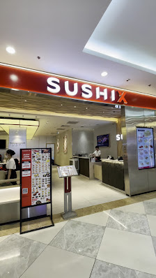 The image shows an interior view of a sushi restaurant named 'SUSHIX'. The establishment has a modern and clean design with white marble flooring, red
