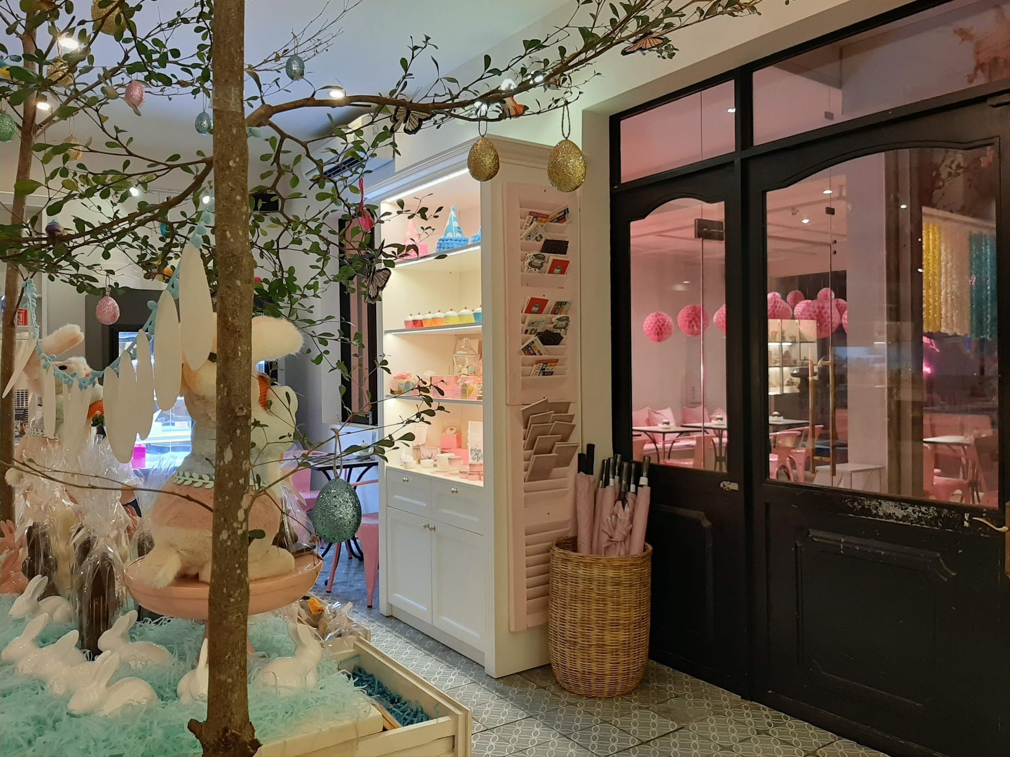 The image depicts the interior of a whimsical venue in Thao Dien, Saigon, featuring a pastel-themed decor. A large tree with hanging ornaments (includ