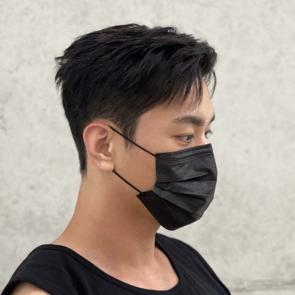 A close-up portrait of a person wearing a black face mask and sleeveless top against an indistinct background.